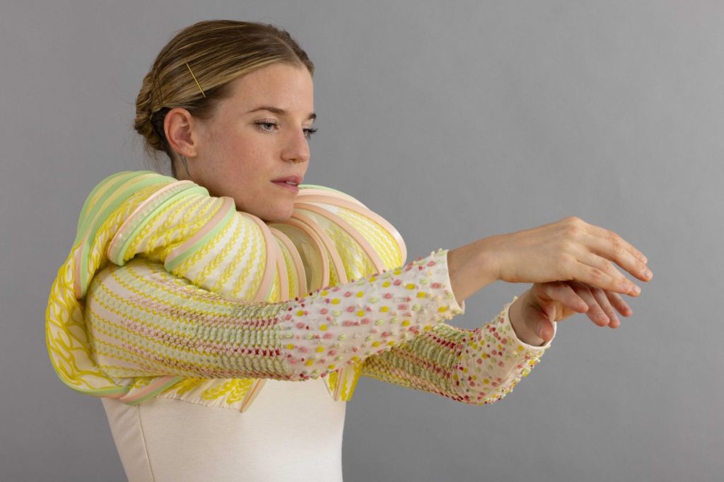Dancer wearing a yellow 3D-printed textile piece that wraps her shoulders and arms